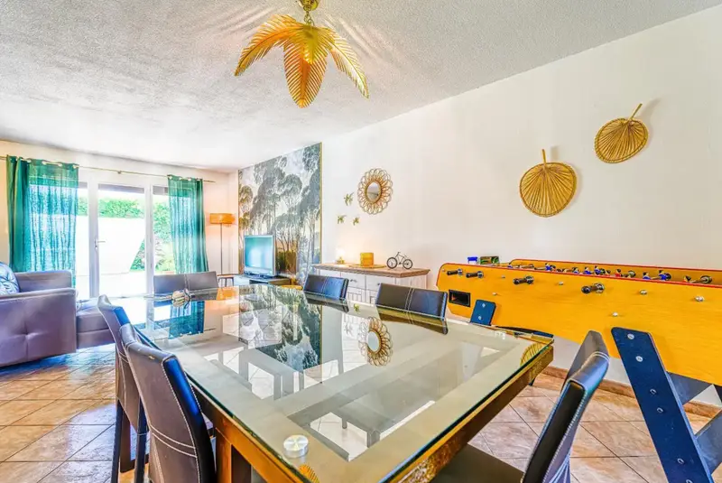 Salon / salle à manger vue sur la piscine avec une grande table à manger pour 8 personnes, un grand canapé d'angle, une TV HD et un babyfoot